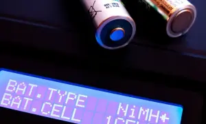 Zwei AA-Akkus, ein Nickel-Metallhydrid-Akku, liegen auf einem Ladegerät. Das Display zeigt "BAT. TYPE NiMH+" und "BAT. CELL 1CELL".