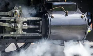 Detail einer Dampfmaschine, die die Kraft der Industrialisierung symbolisiert. Dampf steigt auf und enthüllt die Mechanik.