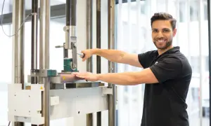 Mann bedient Prüfmaschine zur Ermittlung der Zugfestigkeit von Schrauben. Die Ergebnisse werden in einer Tabelle mit Werten in kg dargestellt.