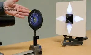 Experiment zur Demonstration des Brewster-Winkels: polarisiertes Licht trifft auf einen schwarzen Würfel, der ein Kreuz aus Lichtpunkten auf einer Leinwand erzeugt.