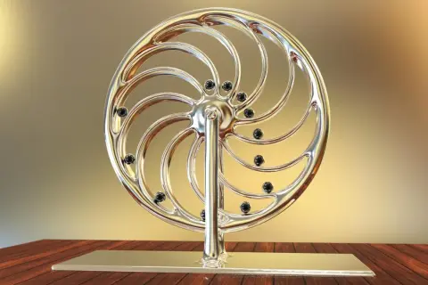 Glänzendes Rad mit schwarzen Kugeln, das an ein Perpetuum mobile erinnert, steht auf einem Holztisch.