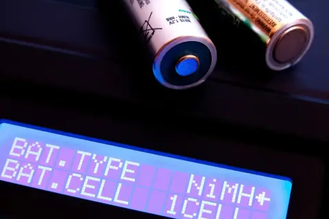 Zwei AA-Akkus, ein Nickel-Metallhydrid-Akku, liegen auf einem Ladegerät. Das Display zeigt "BAT. TYPE NiMH+" und "BAT. CELL 1CELL".