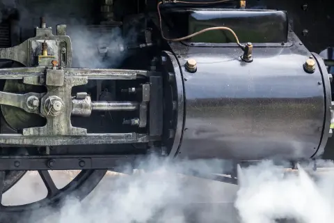 Detail einer Dampfmaschine, die die Kraft der Industrialisierung symbolisiert. Dampf steigt auf und enthüllt die Mechanik.