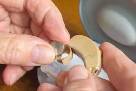 Hände wechseln eine Zink-Luft-Batterie in einem Hörgerät.