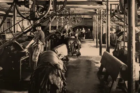 Arbeiter in einer Fabrik, die zeigt, wie funktioniert eine dampfmaschine, mit großen Rädern und Lederwaren.