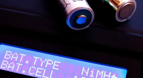 Zwei AA-Akkus, ein Nickel-Metallhydrid-Akku, liegen auf einem Ladegerät. Das Display zeigt "BAT. TYPE NiMH+" und "BAT. CELL 1CELL".