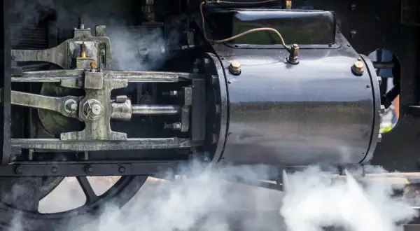 Detail einer Dampfmaschine, die die Kraft der Industrialisierung symbolisiert. Dampf steigt auf und enthüllt die Mechanik.