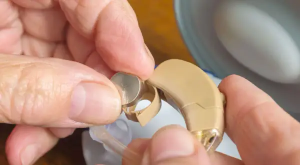 Hände wechseln eine Zink-Luft-Batterie in einem Hörgerät.