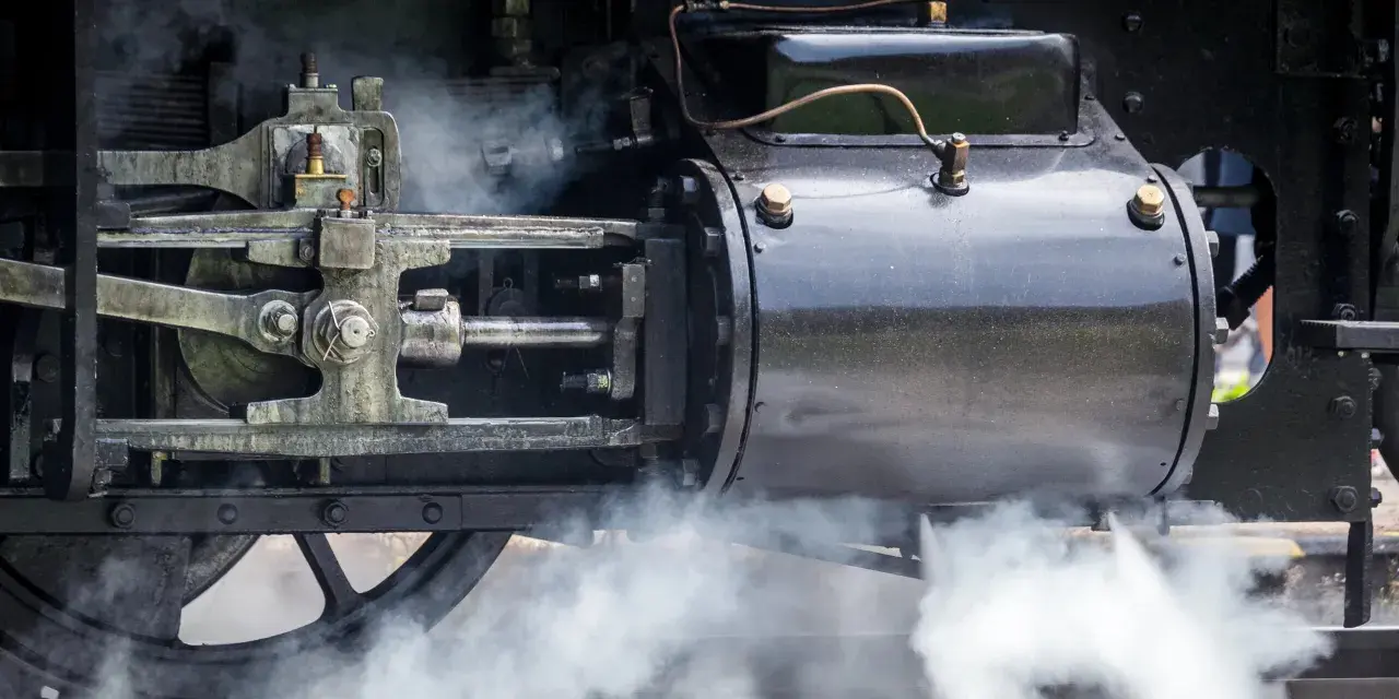 Detail einer Dampfmaschine, die die Kraft der Industrialisierung symbolisiert. Dampf steigt auf und enthüllt die Mechanik.