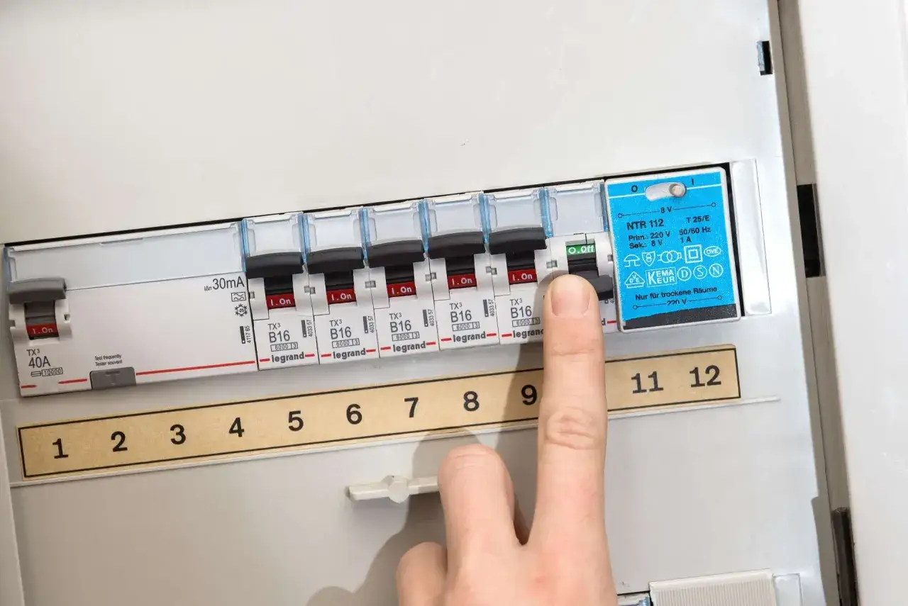 Ein Finger schaltet einen Sicherungsautomaten aus. Die Sicherung ist durchgebrannt, was zu einem Stromausfall führte.