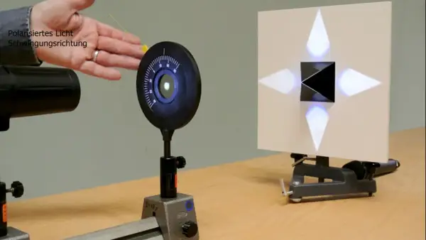 Experiment zur Demonstration des Brewster-Winkels: polarisiertes Licht trifft auf einen schwarzen Würfel, der ein Kreuz aus Lichtpunkten auf einer Leinwand erzeugt.